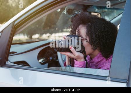 Nahaufnahme einer Fotografin mit Afro-Frisur, die ein Foto mit der Kamera fotografiert, während sie im Auto sitzt. Stockfoto