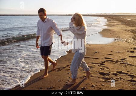 Schönes Paar, das barfuß am Strand mit Händen läuft Stockfoto