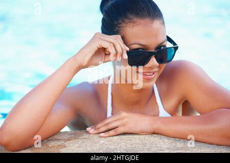 Bereit für einen Sommer Fling. Beschnittene Ansicht einer jungen Frau in einem Swimmingpool, die lächelt und Schatten trägt. Stockfoto