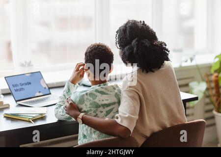 Rückansicht Porträt einer fürsorglichen afroamerikanischen Mutter und Tochter, die zusammen zu Hause studiert und Online-Unterricht über Laptop ansieht Stockfoto