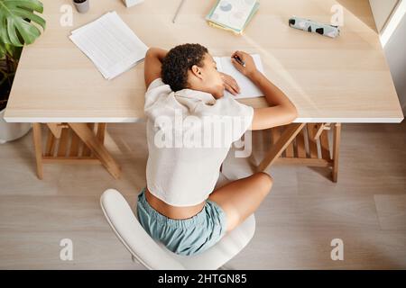 Draufsicht auf das schlafende afroamerikanische Mädchen, das den Kopf auf den Schreibtisch legt, während es mit Hausaufgaben und Kopierraum zu kämpfen hat Stockfoto