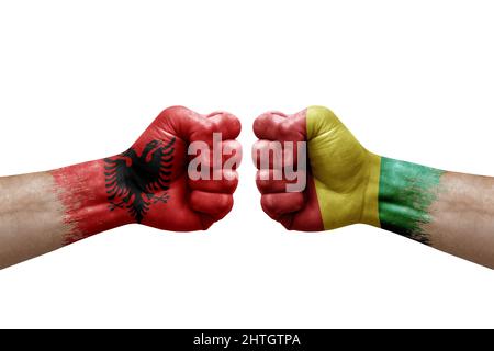 Zwei Hände schlagen sich gegenseitig auf weißem Hintergrund zu. Länderflaggen bemalten Fäuste, Konfliktkrisenkonzept zwischen albanien und Guinea Stockfoto