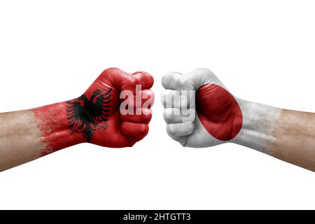 Zwei Hände schlagen sich gegenseitig auf weißem Hintergrund zu. Länderflaggen bemalten Fäuste, Konfliktkrisenkonzept zwischen albanien und japan Stockfoto