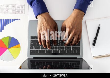 High-Angle-Aufnahme eines nicht erkennbaren Geschäftsmanns, der in einem Büro auf einem Laptop arbeitet Stockfoto