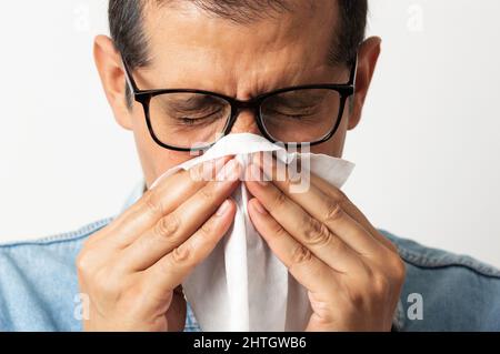 Porträt eines Mannes, der seine Nase mit einem Gewebe vor weißem Hintergrund bläst Stockfoto