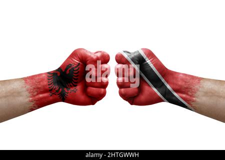 Zwei Hände schlagen sich gegenseitig auf weißem Hintergrund zu. Länderflaggen bemalten Fäuste, Konfliktkrisenkonzept zwischen albanien und tobago Stockfoto