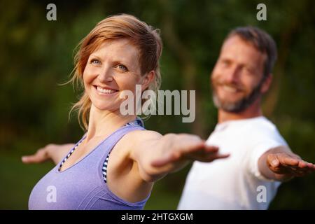 In guter Verfassung bleiben. Aufnahme einer attraktiven Frau, die mit ihrem Partner im Freien Yoga macht. Stockfoto