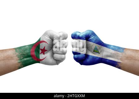 Zwei Hände schlagen sich gegenseitig auf weißem Hintergrund zu. Länderflaggen bemalten Fäuste, Konfliktkrisenkonzept zwischen algerien und nicaragua Stockfoto