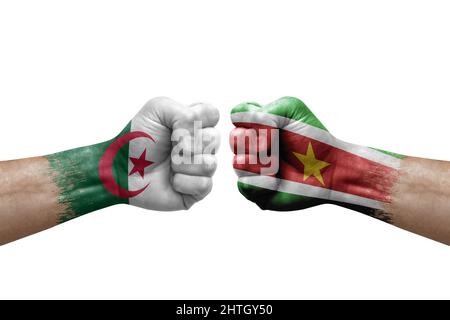 Zwei Hände schlagen sich gegenseitig auf weißem Hintergrund zu. Länderflaggen bemalten Fäuste, Konfliktkrisenkonzept zwischen algerien und surinam Stockfoto