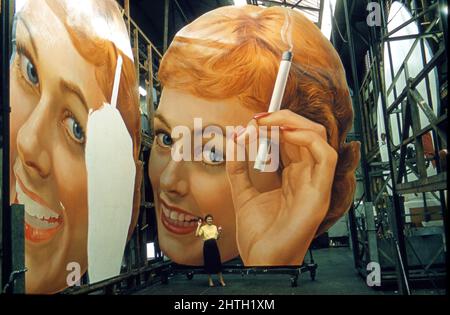 Eine Frau, die eine Zigarette raucht, wird von Werbetafeln in einem Außenwerbestudio in London, England, um 1950s in den Schatten gestellt. Stockfoto