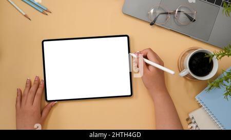 Weibliche Grafikdesignerin skizziert oder macht ein grafisches Bild auf einem Tablet-Computer auf ihrem stilvollen Schreibtisch. Draufsicht, Tablet-White-Display-Modell Stockfoto