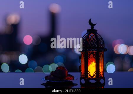 Selektiver Fokus der Laterne, die Mond-Symbol auf der Oberseite und kleine Teller mit Datteln Frucht mit Stadt Bokeh hellen Hintergrund für das muslimische Fest der ho haben Stockfoto