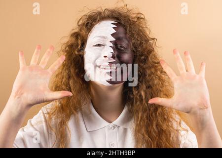 Positive Fan-Football-Frau mit lächelndem, gemaltem Gesicht in der Flagge von Katar, das ihre Handflächen auf gelbem Hintergrund auf die Kamera zeigt. Stockfoto