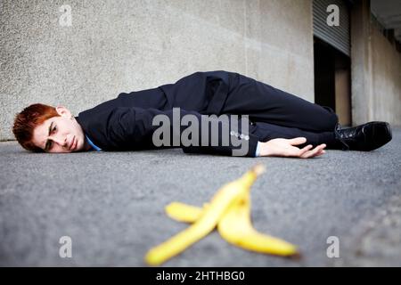 Manchmal sind Bananenschalen unvermeidlich. Ein junger Mann, der auf dem Boden liegt, nachdem er auf einer Bananenschale geschlüpft war. Stockfoto