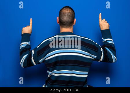 Hispanischer Mann mit zurücktretender Haarlinie, die nach hinten zeigt, mit Finger, Händen isoliert auf blauem Studiohintergrund Stockfoto