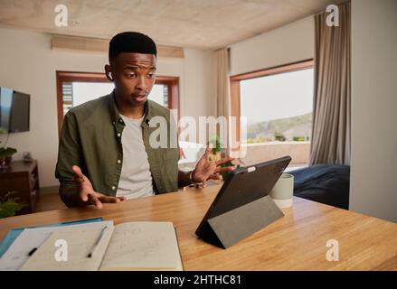 Junger, erwachsener, schwarzer Mann, der Tablet für Online-Anrufe verwendet. Beim Tragen von Ohrhörern ernsthaft reden. Telearbeit von zu Hause aus. Stockfoto