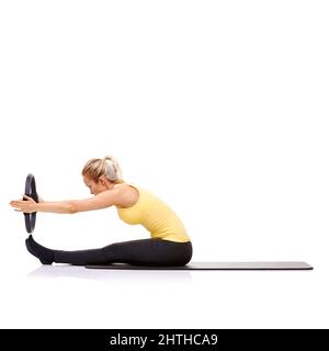Sich selbst ausdehnen. Eine hübsche junge Blondine, die die Roll-up-Übung mit ihrem Pilates-Ring durchführt. Stockfoto