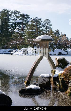 Ishikawa, Japan - 25. Februar 2022: Steinlaterne entlang des gefrorenen Kasumigaike-Teiches in Kenrokuen, einem der schönsten Gärten Japans, im Winter Mo Stockfoto