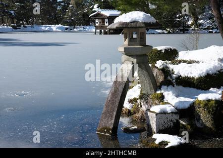 Ishikawa, Japan - 25. Februar 2022: Steinlaterne entlang des gefrorenen Kasumigaike-Teiches in Kenrokuen, einem der schönsten Gärten Japans, im Winter Mo Stockfoto