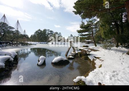 Ishikawa, Japan - 25. Februar 2022: Steinlaterne entlang des gefrorenen Kasumigaike-Teiches in Kenrokuen, einem der schönsten Gärten Japans, im Winter Mo Stockfoto