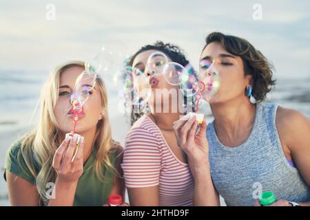 Sprengen Sie Ihre Probleme weg. Kurzer Schuss von drei Freunden, die am Strand Blasen blasen. Stockfoto