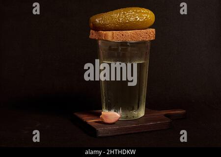 Facettiertes Glas Wodka, Roggenbrot, Knoblauchzehe und eingelegte Gurke Stockfoto