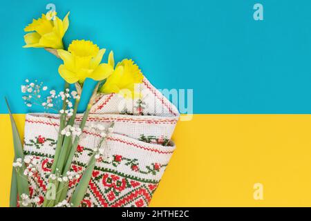 Ukrainische Karte. Ein Blumenstrauß aus Narzissen mit bestickter Serviette auf einem gelb-blauen Hintergrund der Farben der ukrainischen Flagge mit Kopierfläche Stockfoto
