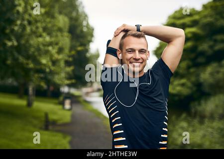 Fitness ist ein wichtiger Bestandteil meines Lebensstils. Porträt eines sportlichen jungen Mannes, der sich vor einem Lauf im Freien dehnt. Stockfoto