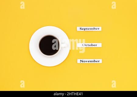 Holzkalender Herbstmonate September Oktober November und Tasse schwarzen Kaffee für Oktober auf gelbem Hintergrund. Konzept Draufsicht Flat Lay Copy Stockfoto
