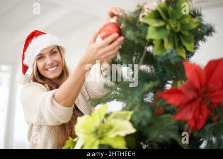 Mein Lieblingsteil des Urlaubs. Eine attraktive Frau, die ihren weihnachtsbaum zu Hause schmückt. Stockfoto