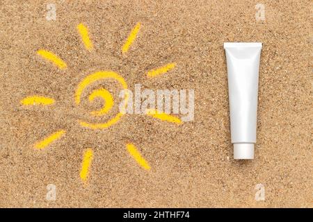 Sonnenzeichen auf Sand und weißem Sonnenschutzrohr gezeichnet. Template-Modell für Ihr Design. Kreative Draufsicht. Stockfoto