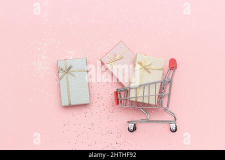 Einkaufswagen, Trolley und Geschenkboxen in Pastellfarben auf rosa Hintergrund, Draufsicht Copy space Concept Verkauf oder Kauf von Geschenken. Stockfoto