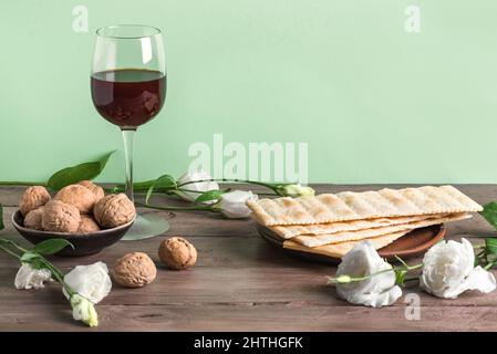 Pesah-Feier-Konzept (jüdischer Passahfeiertag), Kopierraum. Traditionelles Matza-Brot, Walnüsse, Wein und Frühlingsblumen auf einem Holztisch. Stockfoto