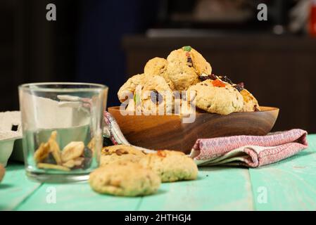Frisch gebackene, weiche Haferflocken-Kekse mit Rosinen, kandierten Früchten, Flachs- und Sesamsamen sowie Walnüssen in Nahaufnahme auf einem Holzteller Stockfoto