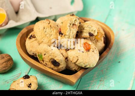 Frisch gebackene, weiche Haferflocken-Kekse mit Rosinen, kandierten Früchten, Flachs- und Sesamsamen sowie Walnüssen in Nahaufnahme auf einem herzförmigen Holzteller Stockfoto