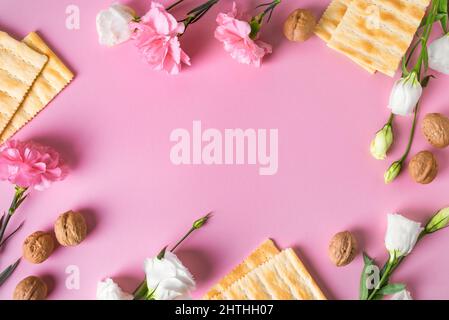 Pesah-Feier-Konzept (jüdischer Passahfeiertag) Rahmen, Kopierraum. Traditionelles Matza-Brot, Walnüsse, Frühlingsblumen auf rosa Pastelltönen. Stockfoto