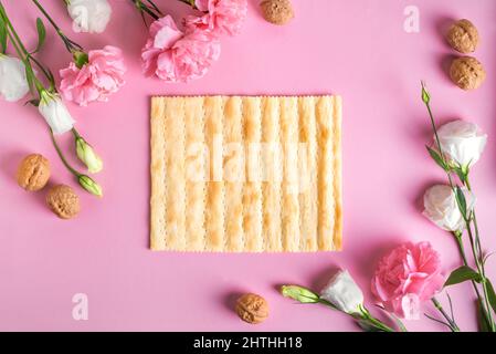 Pesah-Feier-Konzept (jüdischer Passahfeiertag), Kopierraum. Traditionelle Matza-Brot-Textur, Walnüsse, Frühlingsblumen auf rosa Pastelltönen Hintergrund. Stockfoto