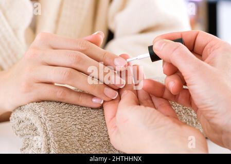 Crop anonyme Maniküre Master Anwendung Nagellack auf den Kunden im Bademantel während der Beauty-Verfahren im Salon Stockfoto