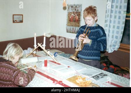 60iger Jahre authentisches Vintage-Foto von einem Jungen, der Trompete spielt und ein Mädchen liest, Schweden. Konzept des Familienlebens, Lernen, Hobbys Stockfoto