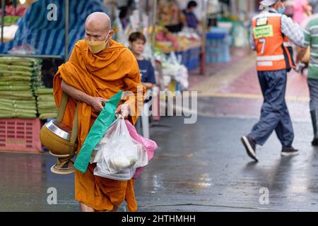 Ein Mönch in einer Straße in Bangkok, Thailand, der seine Almosenschale und seinen Almosenschleppen (Lebensmittelspende) trug, die er während seiner rituellen Almosenrunde am Morgen gesammelt hatte Stockfoto