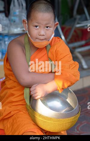 Ein junger, 8 Jahre alter buddhistischer Kindermönch oder Novize während der traditionellen Morgenalmosen, der seine Almosenschale in der Tasche trägt; Bangkok, Thailand Stockfoto