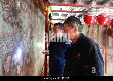 (220301) -- DUNHUANG, 1. März 2022 (Xinhua) -- Su Bomin (R) überprüft die Restaurierung von Wandmalereien in den Mogao-Grotten in Dunhuang, nordwestlich der Provinz Gansu, 23. Februar 2022. Su Bomin, Abgeordneter des Nationalen Volkskongresses (NPC), ebenfalls Dekan der Dunhuang Academy, arbeitet seit drei Jahrzehnten in den Mogao-Grotten, einem UNESCO-Weltkulturerbe in Dunhuang, nordwestlich der chinesischen Provinz Gansu. Su hat seit Beginn seines Dienstes als NPC-Stellvertreter eine Reihe von Vorschlägen zum Schutz kultureller Reliquien unterbreitet. Während der diesjährigen „zwei Sitzungen“, den jährlichen Sitzungen der Natio Stockfoto