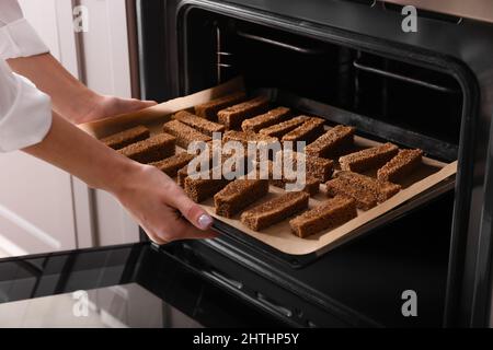 Frau, die Backblech mit Roggencroutons in den Ofen legte Stockfoto