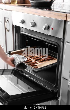 Frau nimmt Backblech mit leckeren Roggencroutons aus dem Ofen Stockfoto