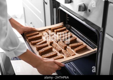 Frau, die Backblech mit Roggencroutons in den Ofen legte Stockfoto