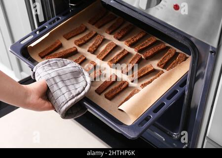 Frau nimmt Backblech mit leckeren Roggencroutons aus dem Ofen Stockfoto