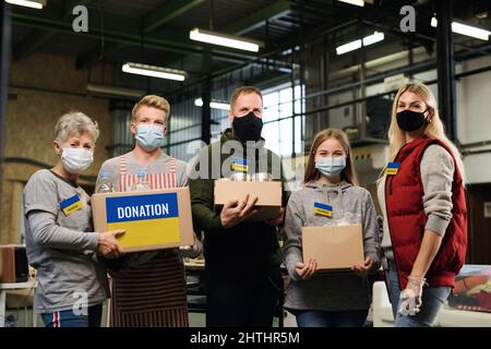 Gruppe von Freiwilligen, die im ukrainischen Flüchtlingszentrum helfen, mit Blick auf die Kamera, russisches Konfliktkonzept. Stockfoto