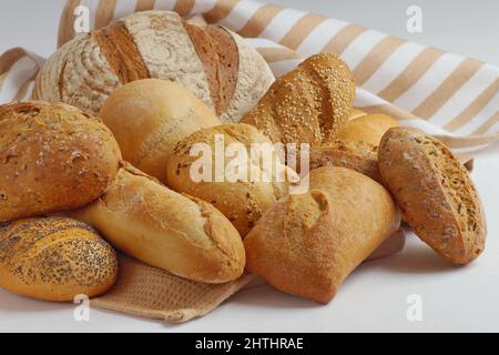 In einem Handtuch, auf einem hölzernen Schneidebrett sind verschiedene Arten von frisch zubereitetem Brot - Rundbrot, Baguette, Ciabatta, Brötchen Stockfoto