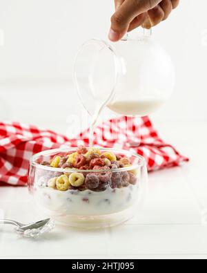 Gieße Milch in die Schüssel mit Froot Loops buntem Müsli. Frühstückskonzept Für Kinder, Weißer Hintergrund Stockfoto