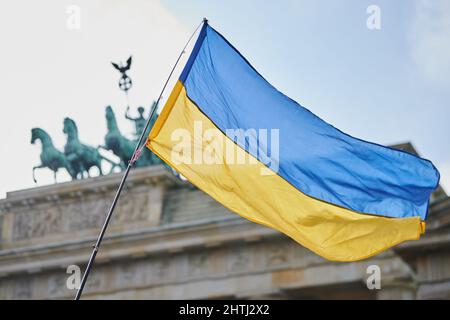 Berlin, Deutschland. 27.. Februar 2022. Die ukrainische Flagge fliegt vor dem Brandenburger Tor, wo sich 100.000 Menschen versammelt haben. Die Demonstration steht unter dem Motto "Stoppt den Krieg! Frieden für die Ukraine und ganz Europa“. Quelle: Annette Riedl/dpa/Alamy Live News Stockfoto